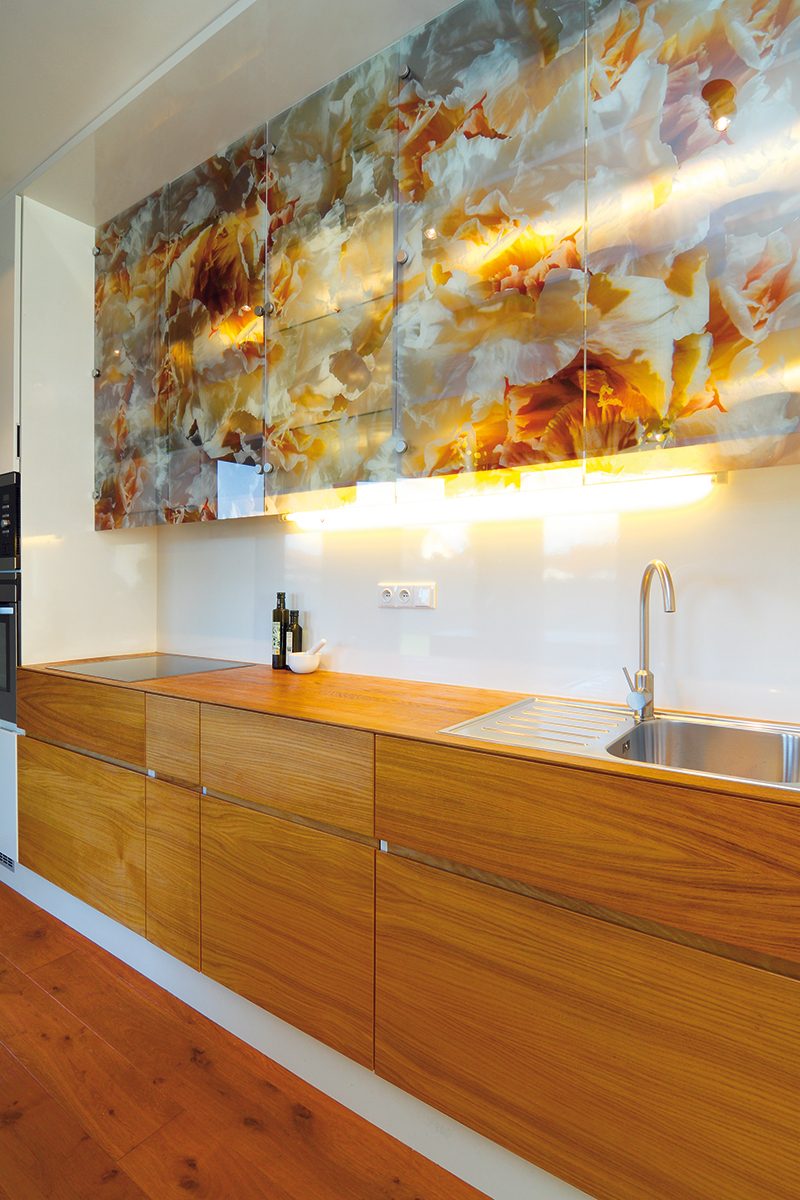 Kuchyň kombinující dřevěnou dýhu, bílé lamino a originální prosklené skříňky s květinovým dekorem je specialitou paní architektky. FOTO: Dano Veselský