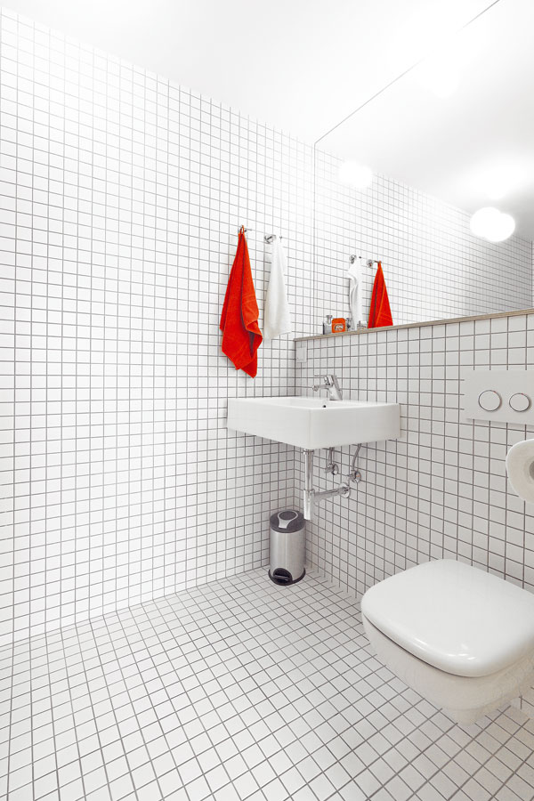  Jednoduchou bílou koupelnu oživuje tmavá spárovka – jak říkají architekti, dodává jí dynamičnost. V koupelně je toaleta a hluboký otevřený sprchový kout. Velké zrcadlo prostor opticky zvětšuje. FOTO: Dano Veselský 