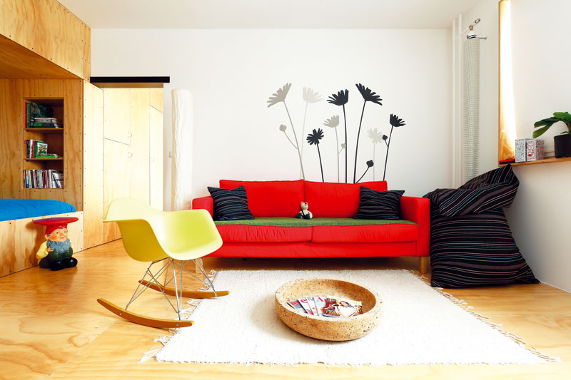 Prostorově úsporné. V neobvykle řešeném bytě je netradičně, ale prakticky „na stojáka“ umístěn i radiátor. Červená pohovka koresponduje s červenou stěnou v kuchyni a dodává jednoduchému, čistému prostoru trochu napětí. FOTO: Dano Veselský 