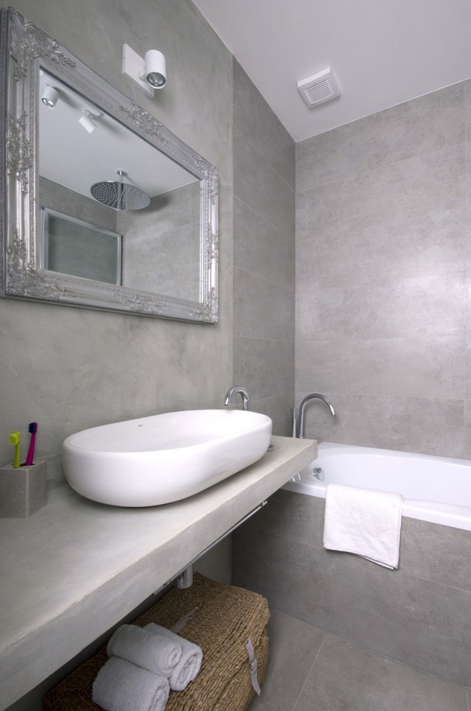 Dekorativní zrcadlo se stříbrným rámem, zavěšené nad oválným umyvadlem „na desku“ ozvláštňuje interiér koupelny.