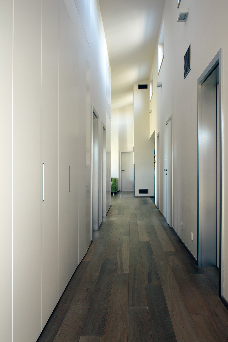 Skříňové mimikry. Na to, aby architektka vytvořila v domě co nejvíce úložných prostor, využila i dlouhou chodbu – nenápadně ji lemují bílé dveře vestavěných skříní na celou výšku prostoru.