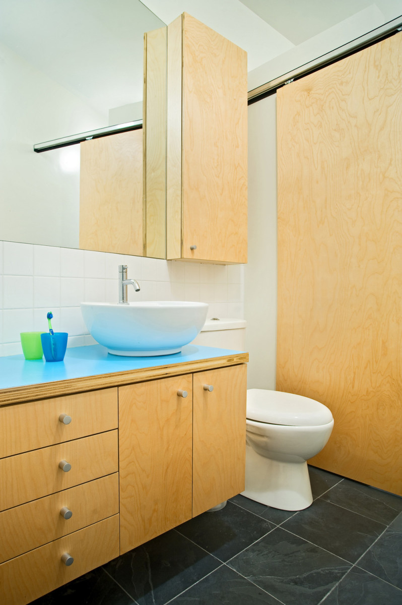 Koupelna je zařízena jednoduše, a to nábytkem vyrobeným na míru z březové překližky. Neutrální barevné spektrum oživuje výrazná modrá deska pod umyvadlem.