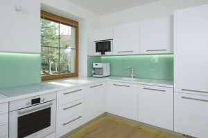 Světlá kuchyně, vybavena bílými kuchyňskými skříňkami s módním mátovým obkladem nad pracovní plochou je praktickým a vkusným řešením.
