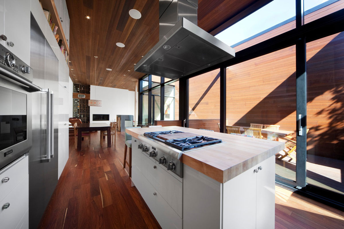 Jednoduché bílé kuchyni s nerezovými akcenty dominuje velký pracovní ostrov s deskou z masivního dřeva. Při práci v kuchyni můžete být v kontaktu nejen s lidmi uvnitř, ale i na terase. Foto: Steve Montpetit