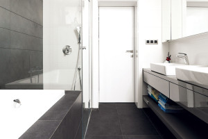 Barevná kombinace šedé a bílé, s několika černými detaily a dřevem, je základem všech interiérů, koupelny nevyjímaje. Takový evergreen.