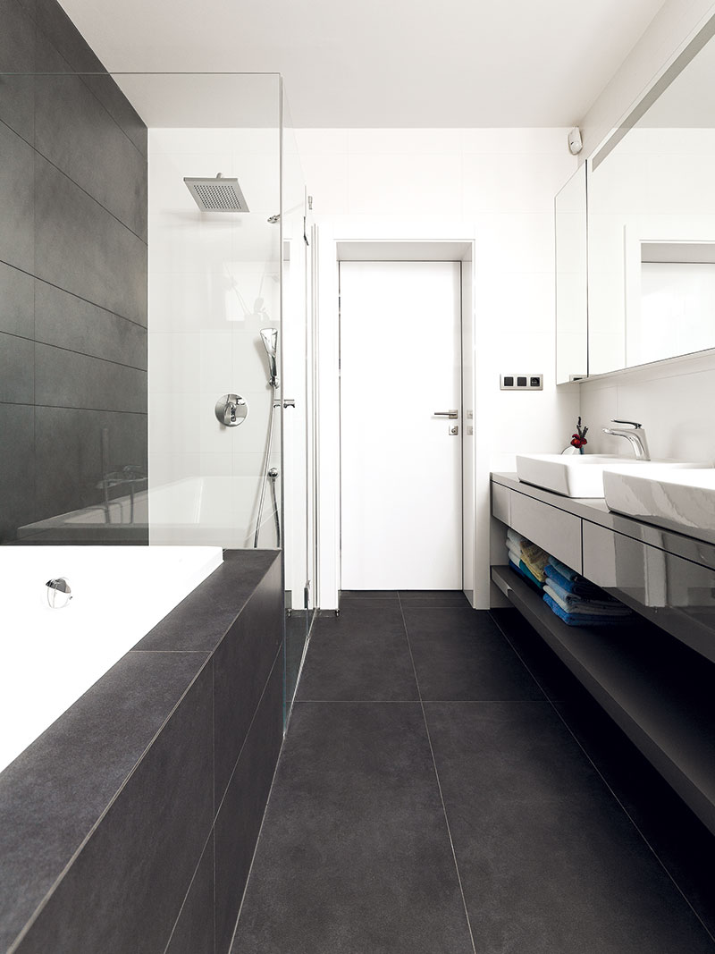 Barevná kombinace šedé a bílé, s několika černými detaily a dřevem, je základem všech interiérů, koupelny nevyjímaje. Takový evergreen.