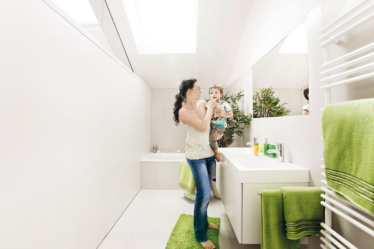 Také v koupelnách vládne minimalismus. Pro dům typická bílá barva je oživena, jak jinak, svěžími zelenými doplňky. Nechybí dvojité umyvadlo nabízející větší komfort zejména během hektičtějších rán.