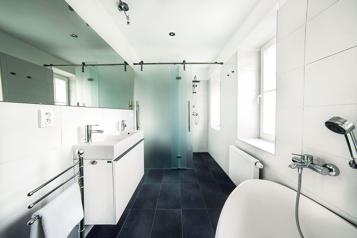 Koupelna se jako jediná vymyká z celkového stylu bytu – má celkem standardní vybavení a čistý, téměř černo-bílý obklad. Vše se nese v duchu jednoduchosti a rozumné investice.