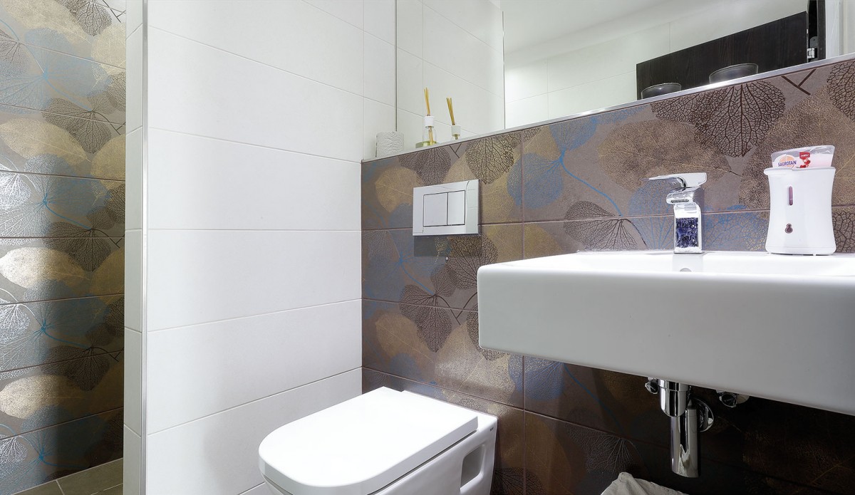 Prostor koupelny oživuje zvolený vícebarevný vzorovaný obklad stěn, který příjemně doplňuje bílou sanitu.