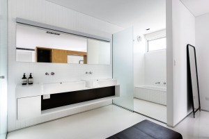 V koupelně a ložnici se opakuje podobné barevné schéma jako například v kuchyňské části. Strohost černobílé opět zjemňují dřevěné prvky, tentokrát v podobě velkého masivního bloku, který je díky pojetí koupelny en suite společný oběma prostorům. V ložnici plní funkci čela a nočních stolků, v koupelně poskytuje úložné prostory… FOTO DMAX