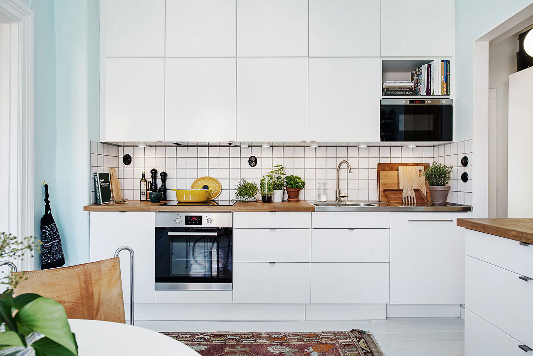 Jednoduchá kuchyňská linka doplněná dřevěnou pracovní deskou a bílou kachlíkovou zástěnou nabízí skutečně štědrý úložný prostor, který dokonale zapadá do prostoru. Foto: Alvhem