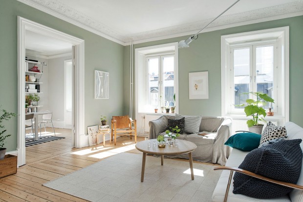 Velký obývací pokoj má světle zelené stěny a je zařízená velmi jednoduše. Poutavým prvkem jsou polštáře s různým vzorováním, které vhodně doplňují světlý nábytek a koberec. Foto: Alvhem