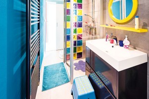 Dětská koupelna jasně ukazuje, kdo je v této místnosti doma. Hravá barevnost doplňků a pestrá sklobetonová zástěna dětem zpříjemňuje koupací rutinu. FOTO WIENERBERGER