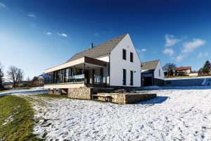 Celý dům je navržen v kombinaci bílé a šedé barvy v několika sytostech. Neutrální světlá barva omítky doplňuje lomový kámen použitý na obložení soklu a dřevěný obklad terasy. FOTO Kamil Saliba