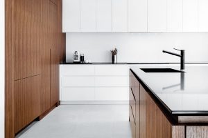 Kombinace bílých skříněk s tmavým dřevem nechává vyniknout minimalismus kuchyně. Dalšími barvami by se tato jednoduchost vytratila. Foto v2com