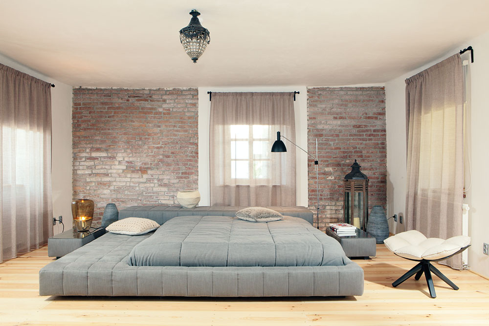 Dominantou spodní ložnice je ikonická postel Squaring Bonaldo. Elegantní místnost doplňuje tlumená barva závěsů, která ladí s cihlovou zdí i polštáři. foto Robert Žákovič