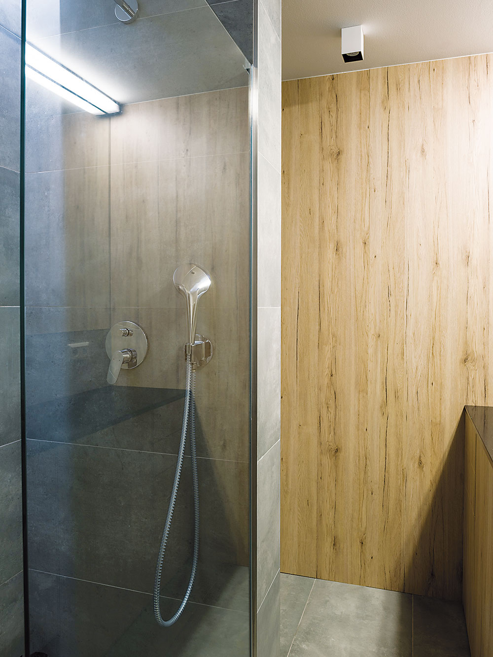Koupelna s WC barevně i materiálově harmonizuje se zbytkem bytu. Místo vany se tu nachází praktický „walk-in“ sprchový kout. FOTO NORA A JAKUB ČAPRNKOVI