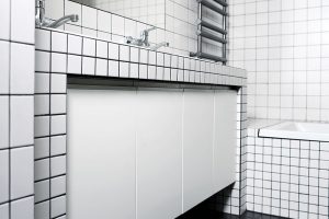 Koupelna je strohá místnost, ve které jsou kombinovány bílé kachličky s tmavou spárou a černé dlaždice. Foto TRAGA