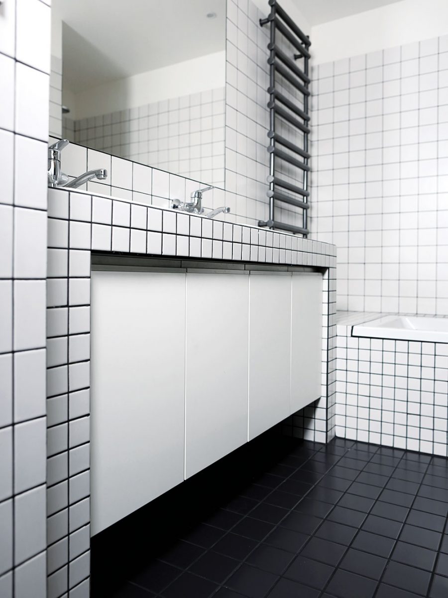 Koupelna je strohá místnost, ve které jsou kombinovány bílé kachličky s tmavou spárou a černé dlaždice. Foto TRAGA