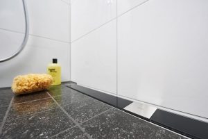 5 Sprchový žlab je harmonicky začleněn do podlahy. Projektant v tomto případě zvolil odtok ke stěně a rám z nerezavějící oceli s designovým roštem z černého bezpečnostního skla. FOTO VIEGA, ROSE BENNINGHOFF