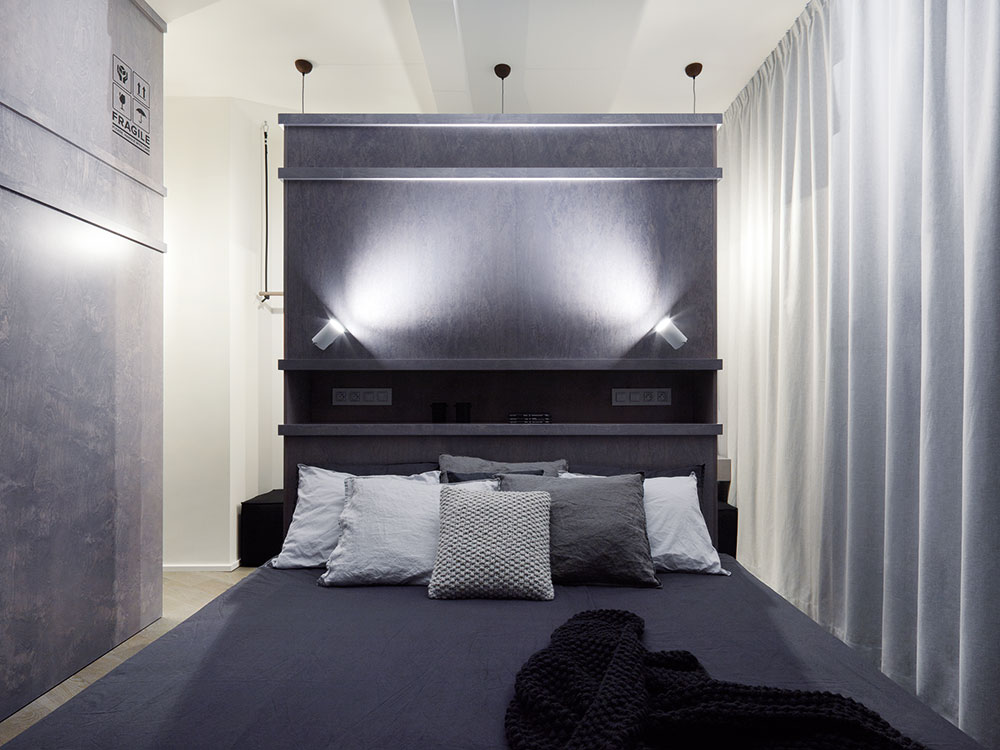 V tmavé ložnici je výrazným prvkem rozměrná postel s vysokým čelem, umístěná doprostřed místnosti, za ní se nachází prostor pro šatnu. FOTO BOYSPLAYNICE