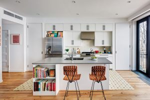 Na knihy narazíte po celém domě, i v kuchyni, která je oproti zbytku interiéru vcelku střídmě zařízená. Neutrální bílou linku ale příjemně doplňují dřevěné barové židličky. FOTO FRANCIS DZIKOWSKI