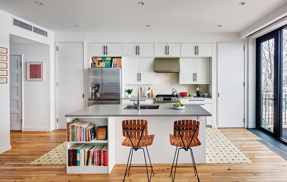 Na knihy narazíte po celém domě, i v kuchyni, která je oproti zbytku interiéru vcelku střídmě zařízená. Neutrální bílou linku ale příjemně doplňují dřevěné barové židličky. FOTO FRANCIS DZIKOWSKI