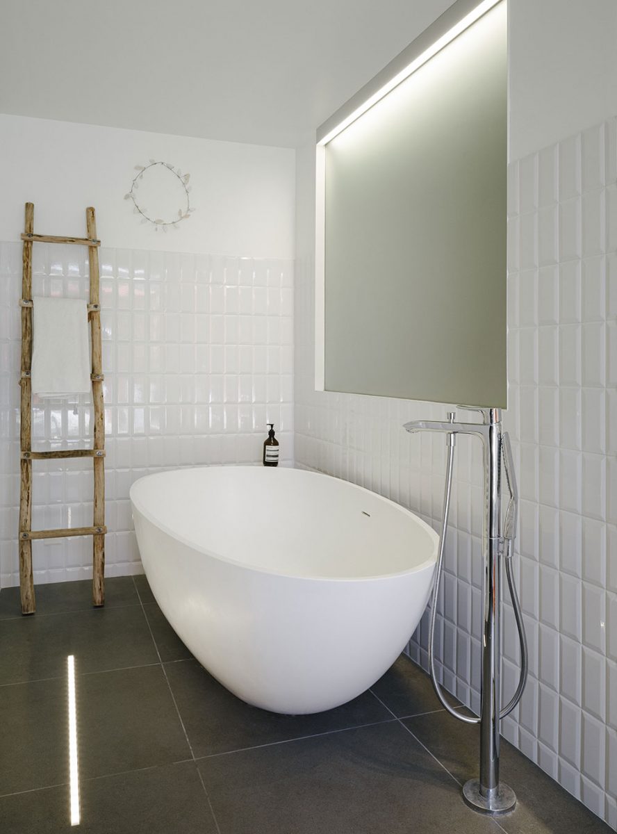 Koupelna s volně stojící vanou je obložena bílým lesklým obkladem. Velkoformátová dlažba opticky zvětšuje prostor. FOTO JULIEN KERDRAON