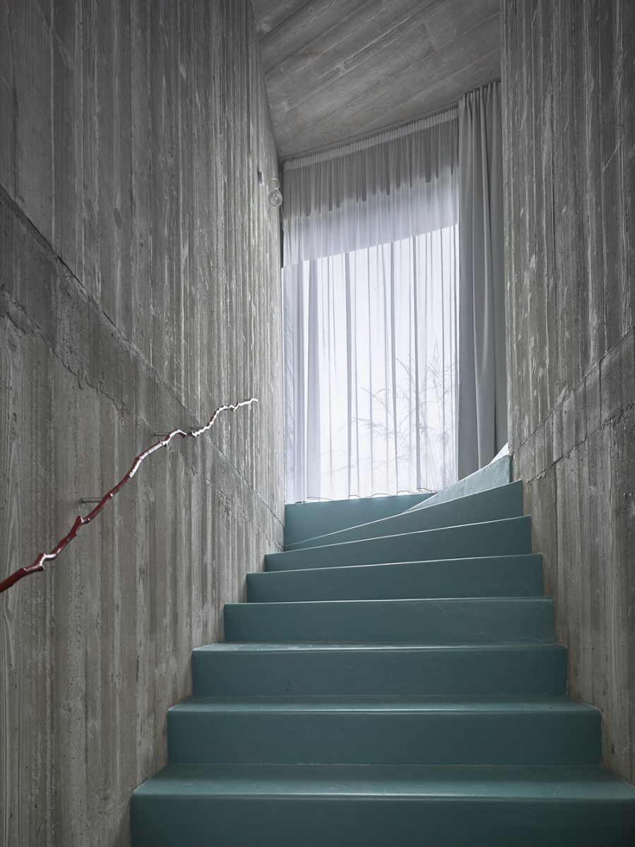 Stěny schodiště jsou tvořené pohledovým betonem, do nějž je vetknuta struktura dřeva. Originální prvek v podobě kovového zábradlí ve tvaru dřevěné větvičky nechybí ani zde. FOTO FILIP ŠLAPAL