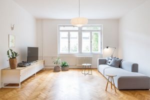 Obývací pokoj je zařízen úsporně, ale velmi funkčně. Základem je minimalistická pohovka v neutrální šedé barvě, subtilní odkládací stolky a televizní skříňka s perforovanými dvířky. FOTO JURAJ STAROVECKÝ