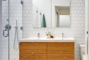 Hlavní koupelna je obložená bílým obkladem a geometrickou dlažbou. Dřevěný prvek ale nechybí. Zde je v podobě čela umyvadlové skříňky. FOTO FRANCIS DZIKOWSKI