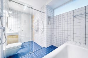 Majitelé chtěli do prostoru koupelny dostat vanu i sprchu. Architekti vytvořili tzv. mokrou zónu uzavřenou skleněnými dveřmi, kde je vyspádovaná podlaha, takže se voda nedostane do suché zóny. Koupelna je obložená obkladem 10 x 10 cm a vyspárovaná modře. FOTO BENEDIKT MARKEL A DOMINIK KUČERA