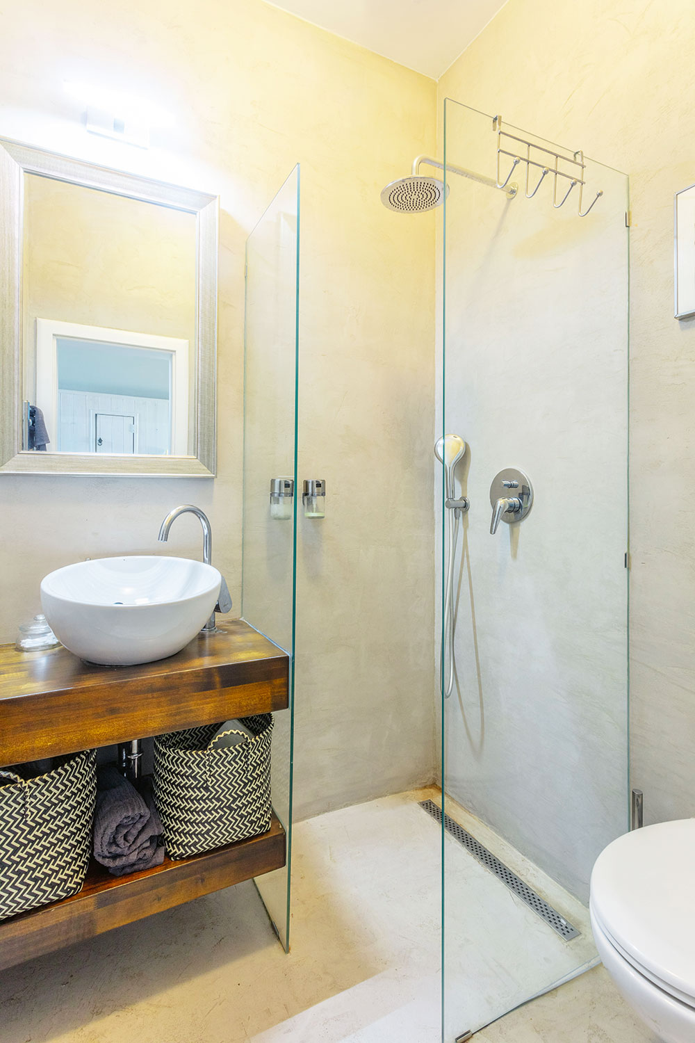 Rekonstrukce koupelny je nejnovějším počinem. Betonová stěrka zakrývá původní křiklavě červené obklady, které působily divoce a nepatřičně. Vybavení je střídmé v barvě teakového dřeva. Zrcadlo ve zdobeném rámu pak stylově propojuje koupelnu se zbytkem domu. FOTO JIŘÍ HURT