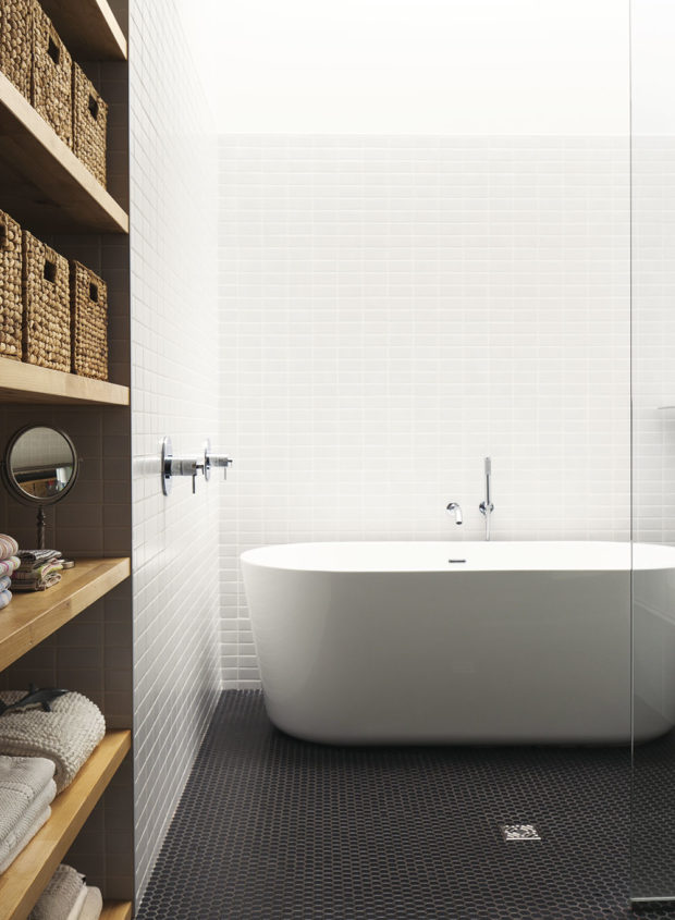 Bílé obložení stěn doplňuje černá mozaiková dlažba a přírodní dřevo na vodorovných plochách koupelny