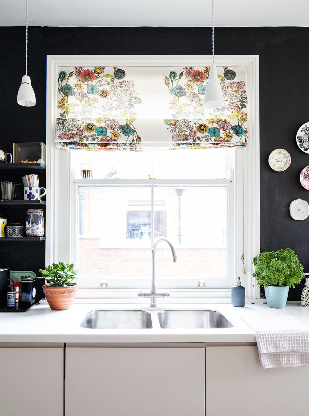 Bílé kuchyňské skříňky a linka kontrastují s černě zabarvenou stěnou.