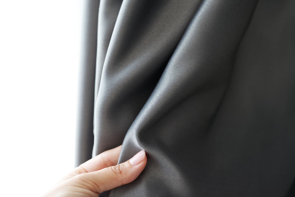 Woman’s hand touching curtain, gray blackout fabric, light-blocking fabric