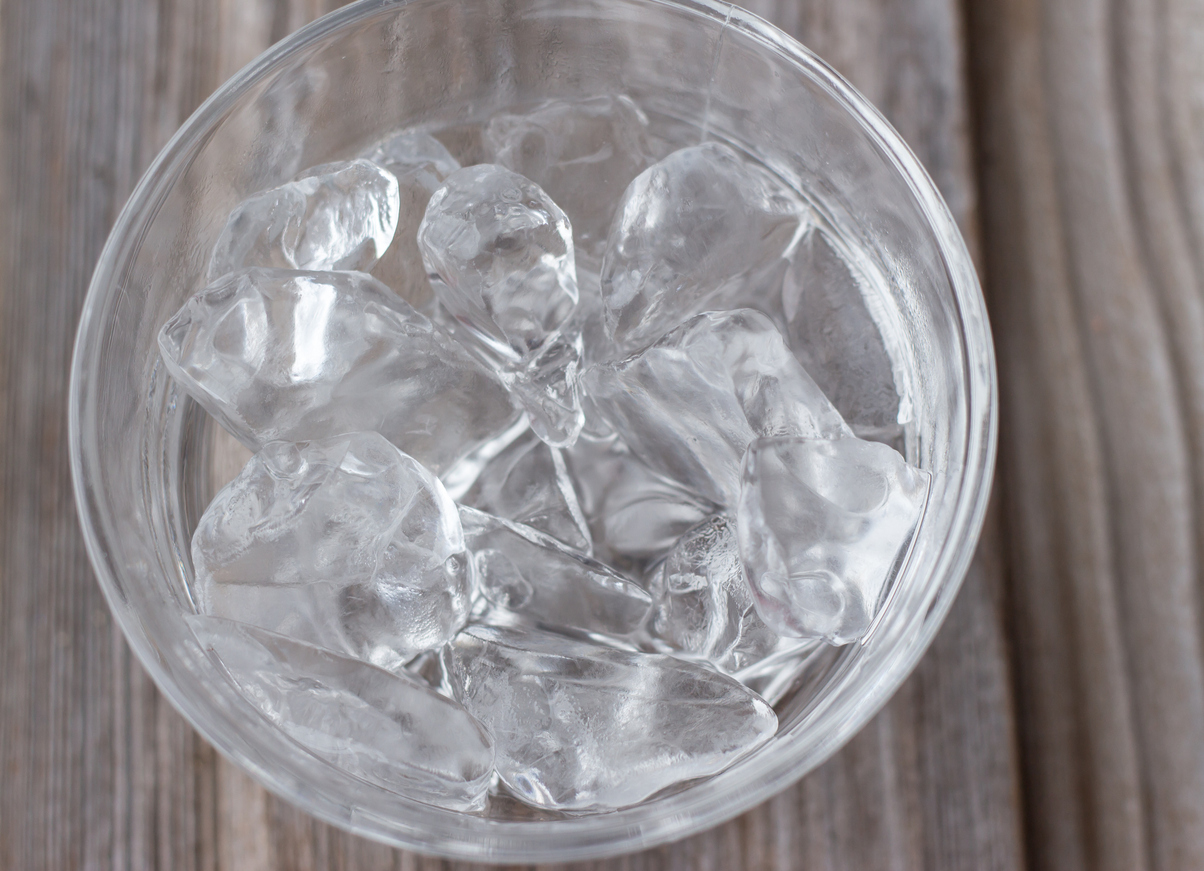 Clear glass bowl with ice cubes on wood background