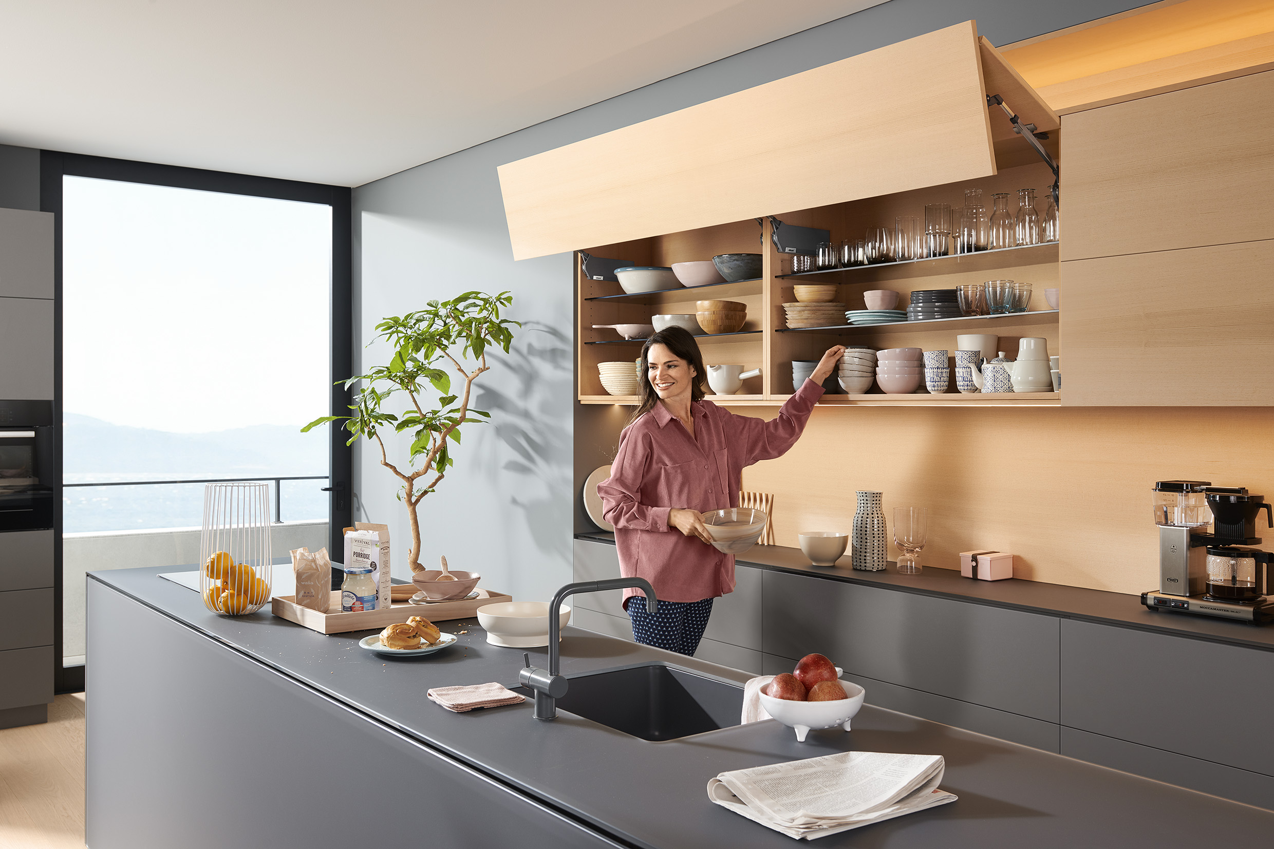Žena v moderní kuchyni otevírá vrchní police