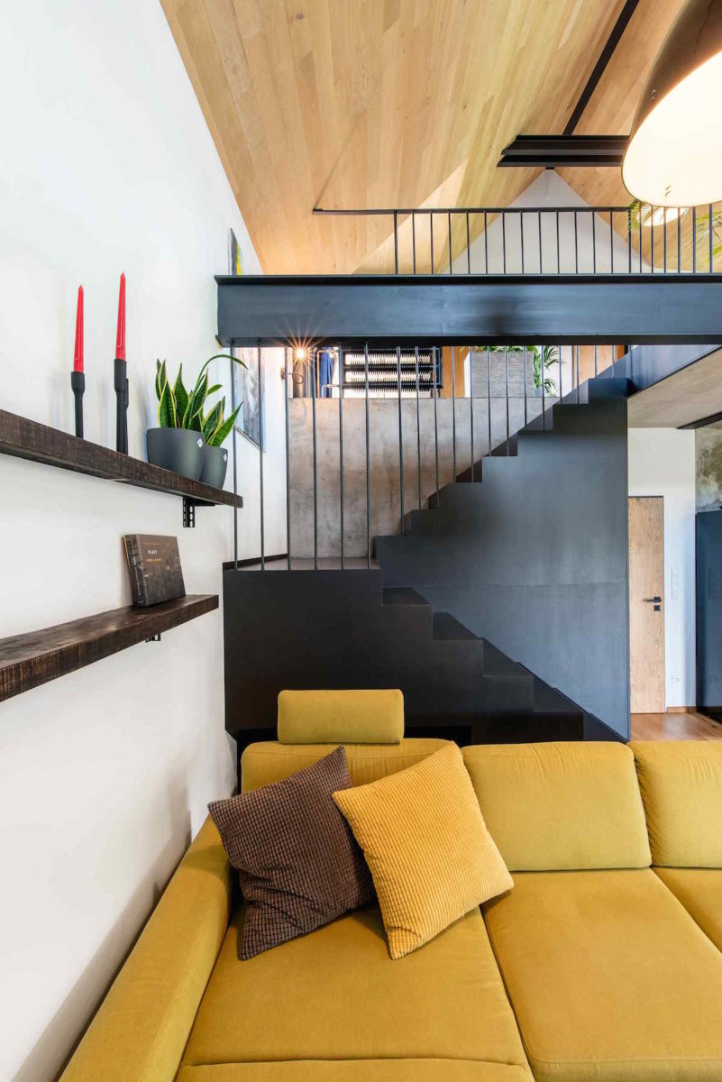 Obývací část s černým schodištěm a žlutým gaučem