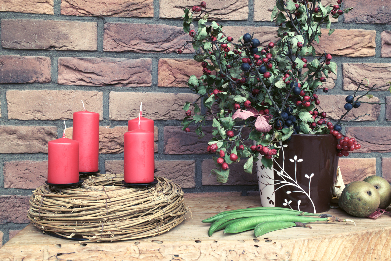 Christmas wreath, nature style, on the wooden table with decorations. Wild berries in vase, vintage, victorian England brick wall behind it.