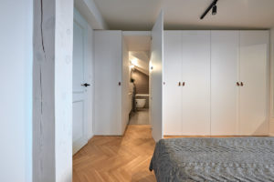 Jednoduchá bílá ložnice s parketami a koupelnou v skříni