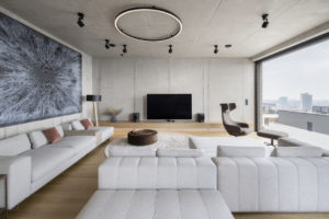 Betonová obývací část s velkým světllým gaučem a moderním dílem
