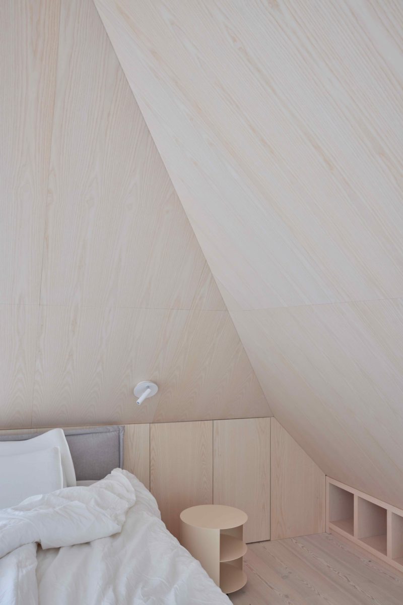 Podkrovní ložnice obložena světlým dřevem se šikmou stěnou
