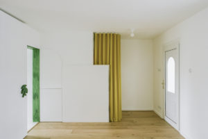 Bílý interiér bytu se zelenými rámy a žlutým závěsem