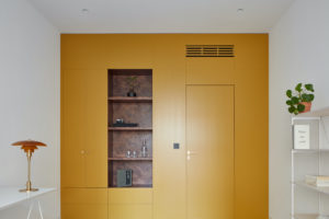 Žlutá stěna s mramorovými policemi a vstupem do koupelny