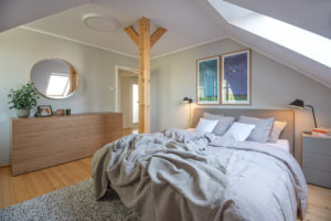 Moderní podkrovní ložnice s velkou postelí a dřevěným stĺpem