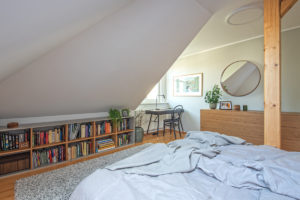 Moderní podkrovní ložnice s velkou postelí a dřevěným stĺpem