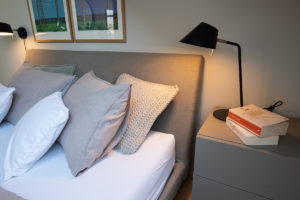 Čalouněná postel se šedým stolkem a lampou