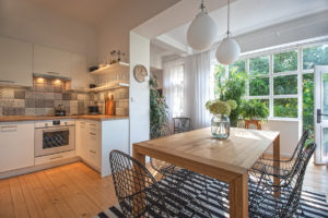 Otevřený prostor v domě s bílou kuchyní a dřevěnou podlahou a rostlinami