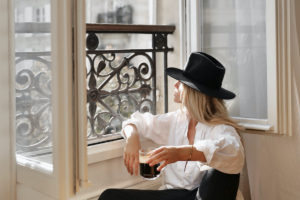 Žena v klobouku sedící ve francouzském okně